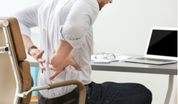 a man holding his back in pain while sitting on his chair at work