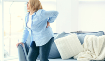 a woman standing up from sitting on her couch holding her back in pain