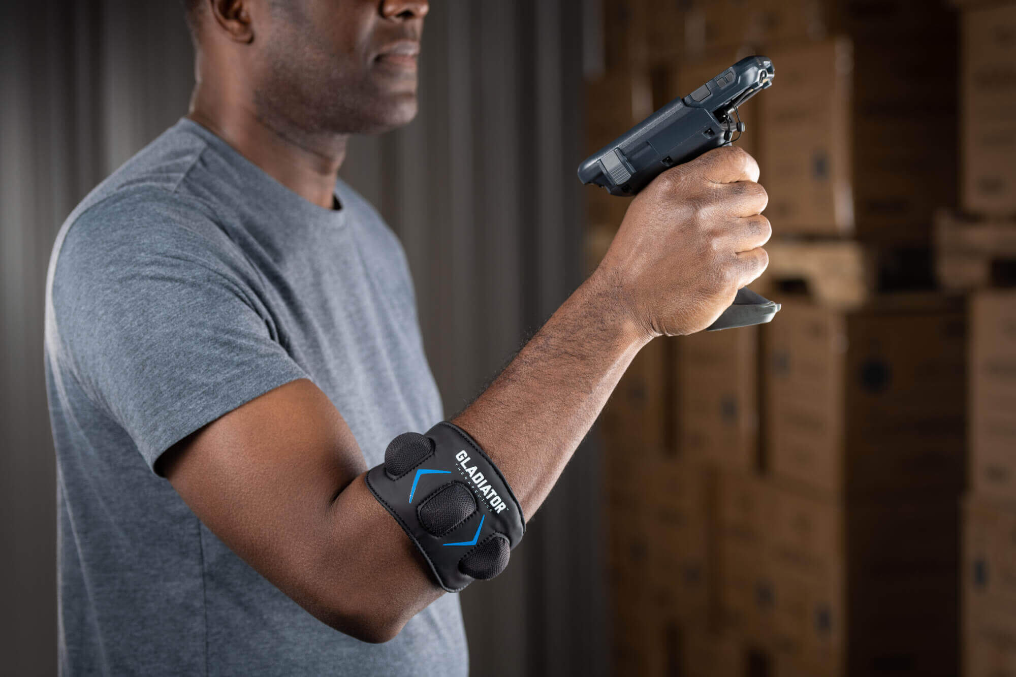 Gladiator Therapeutics Elbow Device A man holding a phone wearing a Gladiator Therapeutics Elbow Device.